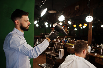 Handsome bearded man at the barbershop, barber at work, using hair dryer.