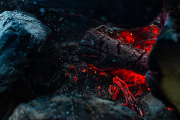 Smoldered logs burned in vivid fire. Atmospheric background with orange flame of campfire. Unimaginable detailed image of bonfire from inside with copy space. Smoke and ashes close up.