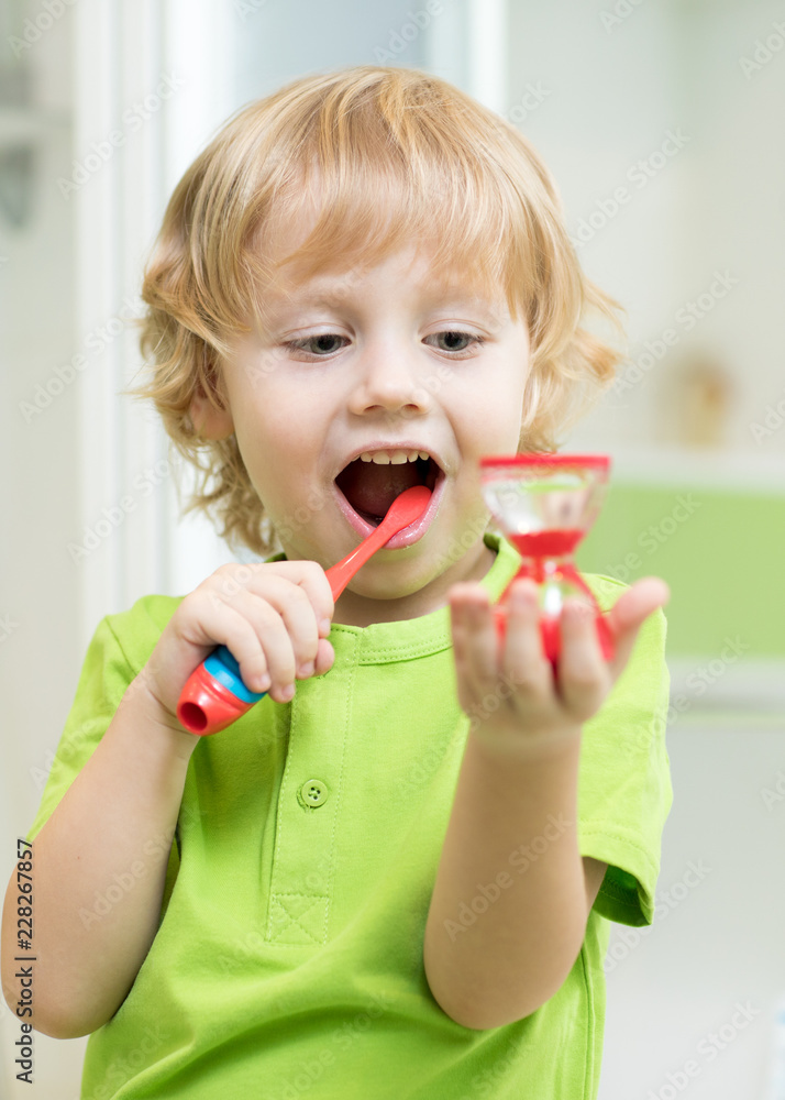 Canvas Prints Little child boy brushing his teeth and looking at hourglass