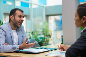 Confident Hispanic man discussing marketing ideas with colleague. Serious enterprising businessman gesturing hand with pen while explaining his plan at meeting. Teamwork concept