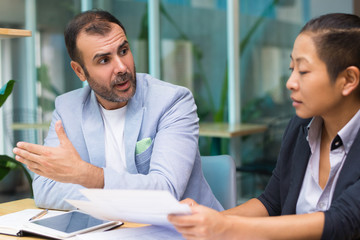 Shocked Hispanic male manager explaining business strategy to Asian colleague. Puzzled man...