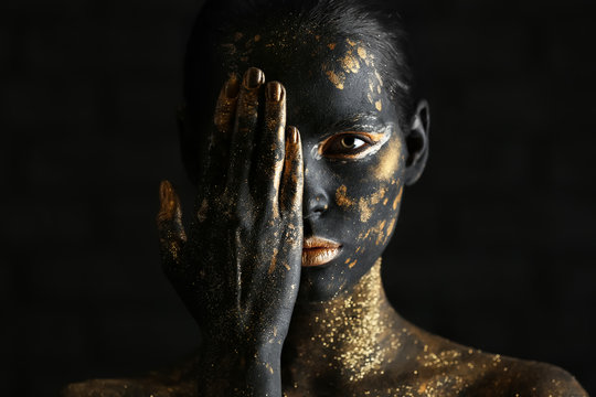 Beautiful woman with black and golden paint on her body against dark background