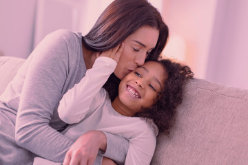 Mothers love. Delighted nice woman hugging her daughter while giving her a kiss