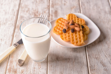 Glass of milk and plate with waffles on wooden table