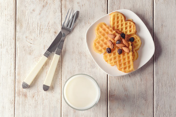 Glass of milk and plate with waffles on wooden table