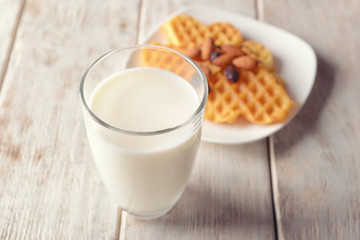 Glass of milk and plate with waffles on wooden table