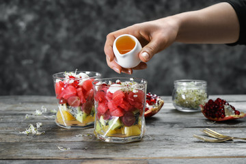 Woman adding honey into glass with tasty watermelon salad on wooden table