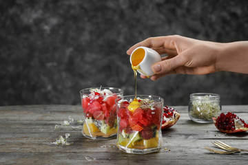 Woman adding honey into glass with tasty watermelon salad on wooden table