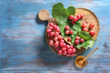 Ripe grapes and bowl with honey on wooden table