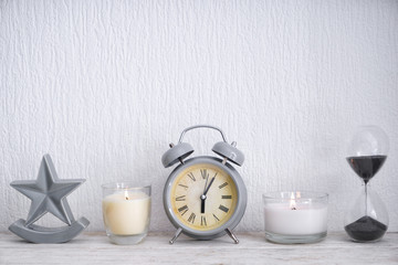 Beautiful burning candles with alarm clock and hourglass on light wooden table
