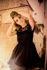 Beautiful blonde girl with big blue eyes and black dress, looking pensive with her hands in the hair, next to an old wall