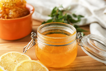 Jar with honey and lemon slices on wooden table, closeup