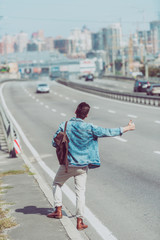 back view of man hitchhiking alone on road