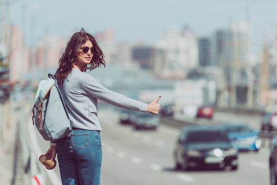 young woman with backpack and coffee to go hitchhiking at road