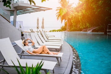 Asian woman relaxing by the pool in a luxurious beachfront hotel resort at sunset enjoying perfect...