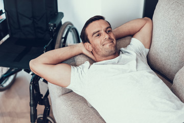 Smiling Handsome Man Lies on Sofa Near Wheelchair