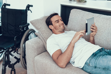 Man Relaxing on Sofa with Tablet near Wheelchair