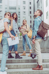 group of young tourists with backpacks standing on street in new city