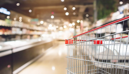 Empty red shopping cart with abstract blur supermarket discount store aisle and product shelves interior defocused background