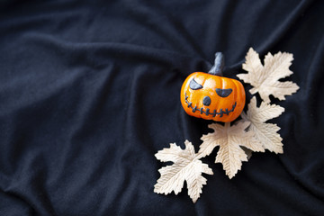 Design funny Halloween pumpkin with paper leaves on black fabric texture background, Halloween decoration item