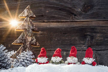 Vier Weihnachtsmänner in der Adventszeit vor Holzwand im Sonnenschein