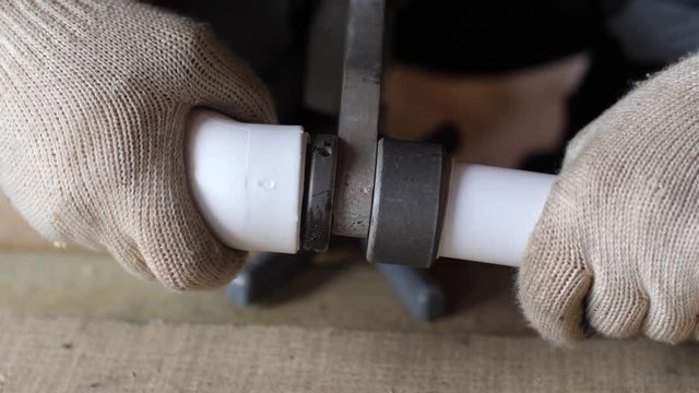 Hands in gloves soldering plastic pipes to connect them together. 4k 60fps slow motion. Brazing of pipes made of polycarbonate with a special iron. Plumbing work. Close up