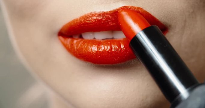 Woman applying lipstick. Young model putting on some makeup, using lipstick to color hel lips - beauty concept closeup 4k