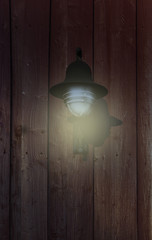 Holzwand mit leuchtender Wandlampe in der Abenddämmerung