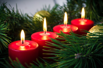 four red lit advent candles surrounded by green fir branches