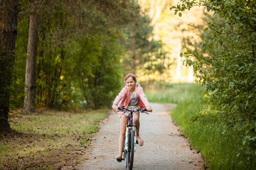 Naklejka premium Little girl is riding the bicycle looking in the camera and smiling in the park at evening