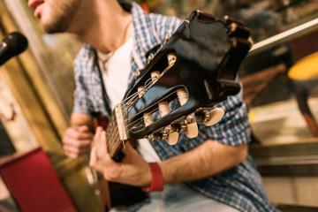 Feel sound. Close up of shiny wooden headstock and man singing and playing guitar