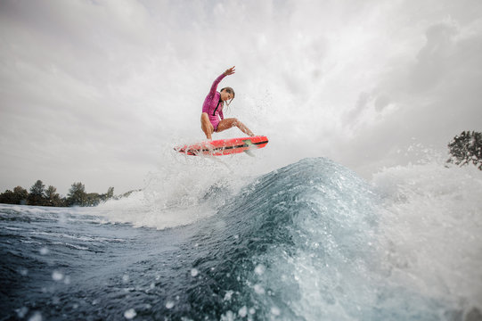 Active woman wakesurfer jumping up the blue splashing wave against sky