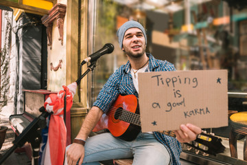 Little reward. Talented male musician holding cardboard with inscription and begging