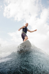 Young wakesurfer standing on the high blue wave