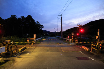 Train crossing gates closed on Japanese rural road at sunset