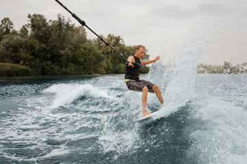 Active man riding on the wakeboard holding a rope