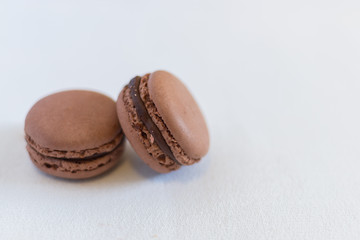 Two brown chocolate macarons stacked on a white illuminated background