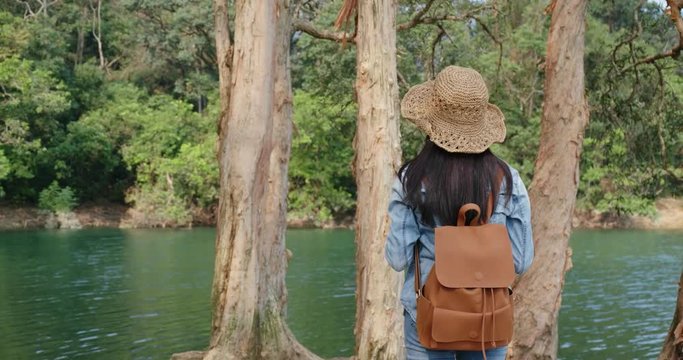 Woman sit on the tree root and enjoy the view of the lake