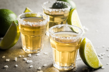 Macro photo of shots of gold Mexican tequila with lime and salt on wooden rustic background....