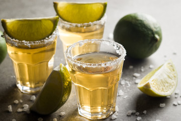 Macro photo of shots of gold Mexican tequila with lime and salt on wooden rustic background....