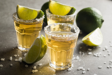 Macro photo of shots of gold Mexican tequila with lime and salt on wooden rustic background....