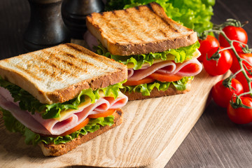 Close-up van twee sandwiches met spek, salami, prosciutto en verse groenten op rustieke houten snijplank. Clubsandwich-concept.