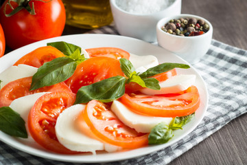 Photo of Caprese Salad with tomatoes, basil, mozzarella, olives and olive oil on wooden background. Italian traditional caprese salad ingredients. Mediterranean, organic and natural food concept.