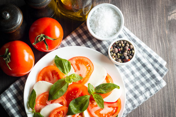 Photo of Caprese Salad with tomatoes, basil, mozzarella, olives and olive oil on wooden background. Italian traditional caprese salad ingredients. Mediterranean, organic and natural food concept.