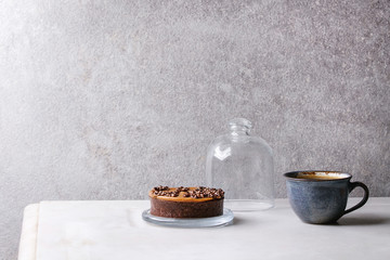 Obraz na płótnie Canvas Sweet chocolate tartlet with cup of coffee espresso standing on white marble table with grey wall at background. Minimalist style. Copy space