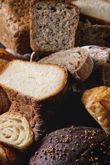 Variety of fresh baked rye, spelled, wheat craft artisan bread, whole and sliced, on black texture background. Close up