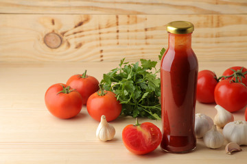 Red sauce in a bottle with fresh ingredients, tomatoes, pepper and garlic on a natural wooden background. With space for inscriptions