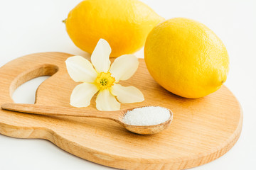 two lemons, a wooden spoon with salt and a flower of narcissus on a wooden board 
