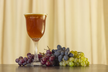 glass of dark unfiltered beer on a beige background with bunches of pink, black and white grapes