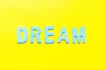 Word DREAM made out of small blue wooden letter on yellow background, flat lay